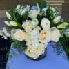 Low arrangement of ivory roses, tulips, orchids, and hydrangeas in a glass vase with trailing greenery