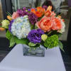 Low arrangement of bright mixed flowers in a clear glass cube vase