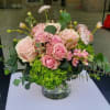 Low arrangement of pink roses and spray roses with bright green hydrangea in a clear glass vase