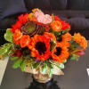 Bright orange sunflower and rose arrangement with succulent in a glass vase