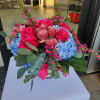 Low glass vase arrangement with hot pink roses and blue hydrangeas accented by small pink blossoms.