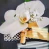 White orchid wrist corsage with small white blooms, gold ribbon, and rhinestone bracelet.