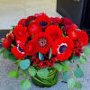 Low arrangement of vivid red flowers with dark centers in a leaf-wrapped glass vase