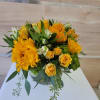 Low arrangement of yellow roses and yellow flowers in a round glass vase on a white table