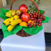 Wicker basket filled with assorted fresh fruit including bananas, apples, grapes, and a pineapple.