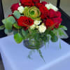 Low round arrangement of red and white roses with a green succulent in a clear glass bowl vase