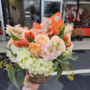 Low bouquet of peach roses, orange tulips, and white hydrangeas in a clear round vase with an orange card.