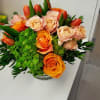 Low arrangement of orange and peach roses with orange tulips and green hydrangea in a clear glass vase
