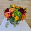 Low glass vase of orange, yellow, and red roses with bright green hydrangea