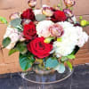 Low round arrangement of red and blush roses with white blooms in a clear glass vase