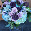 Lavender roses and deep purple blooms arranged with blue hydrangeas in a rounded bouquet