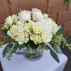 Low round arrangement of white roses, hydrangeas, and peonies in a clear glass vase