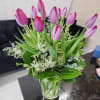 Bouquet of pink and purple tulips arranged in a clear glass vase on a table