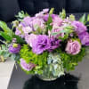 Low round arrangement of purple and lavender flowers in a clear glass bowl vase