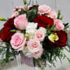 Round arrangement of red and pale pink roses with white blooms in a pink glass vase