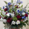 Basket arrangement of red roses, white daisies, and blue flowers