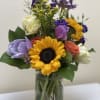 Mixed bouquet with a sunflower, roses, and purple blooms in a glass vase