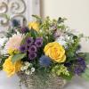 Mixed flower arrangement in a woven basket with yellow roses and purple blooms