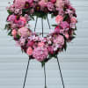 Heart-shaped floral wreath on a black stand with pink and purple blooms