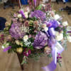 Large bouquet of purple hydrangeas, roses, and white flowers with a lavender ribbon