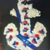 Floral arrangement shaped like a cross with white flowers, red roses, and blue ribbon