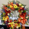 Large floral wreath with roses, gerbera daisies, and mixed blooms on a stand