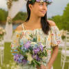 Woman holding a purple, blue, and white bouquet and wearing a matching floral crown outdoors