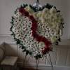 Heart-shaped floral wreath with white daisies and red roses on a stand