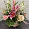 Pink lilies and roses arranged in a low vase with white filler flowers.