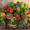 Low floral arrangement with orange roses and red blooms in a decorative container