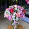 Pink roses, lavender daisies, and white blooms in a clear glass vase with a pink ribbon.