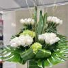 Tall modern arrangement of white roses and green hydrangeas in a square glass vase with large tropical leaves.