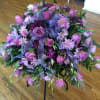 Pink and purple floral arrangement on a black stand with ribbon