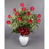 Red roses arranged in a white vase with baby's breath and a red ribbon