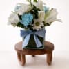White lilies and daisies with blue carnations in a glass vase with a blue ribbon