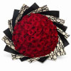 Large round bouquet of red roses wrapped in layered black and cream patterned paper