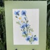 Framed floral embroidery with blue and white flowers on a pale green mat