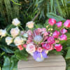 Pink and white roses arranged in a white vase with a purple ribbon