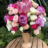 Pink and white roses arranged in a tall vase with a large pink protea