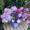 Pink and white roses arranged in a white bucket with a purple ribbon