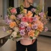 Large pastel bouquet in a pink hat box held by a man indoors