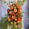 Tall orange and peach standing floral spray with roses and lilies on an easel.