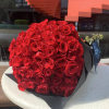 Large bouquet of tightly packed red roses wrapped in black paper with a blue ribbon