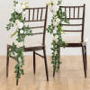 Pair of dark chairs decorated with cascading white and cream rose garlands with lush green foliage