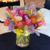 Bright mixed tropical and protea flower arrangement in a clear glass vase with stones.