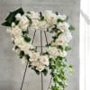 Heart-shaped wreath of white roses with trailing ivy on a black easel stand