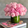 Tight cluster of pink peonies in a green cylinder vase set on a floral coffee table book