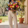 Woman holding a large mixed bouquet of bright roses and daisies in a clear glass vase