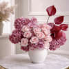 Pink rose, hydrangea, and orchid arrangement with burgundy accents in a white vase on a marble table