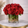 Low arrangement of red roses in a clear glass cylinder vase with stones on a small round table